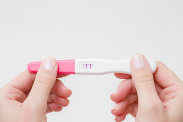 Young woman's hands holding pregnancy test with two stripes on gray background. Positive result. Closeup. Point view shot. Empty place for text.  - obrazy, fototapety, plakaty