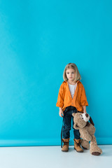 serious and adorable kid holding teddy bear on blue background