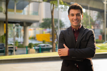 Young happy Hispanic businessman smiling with arms crossed outdoors