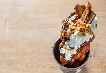 Hong Kong bubble waffles with ice cream, nuts, chocolate, cookies on wooden table background