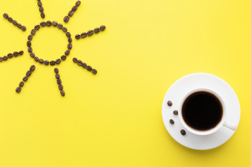 White cup of black coffee on bright yellow table. Wake up with morning coffee. Sun shape created from brown beans. Empty place for inspirational, motivational text, quote or saying. 