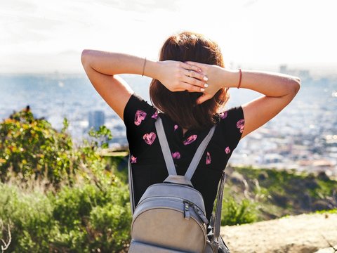 Girl with long hair photographed from behind, sitting on a hill and looking at the panorama of Los Angeles in the summer