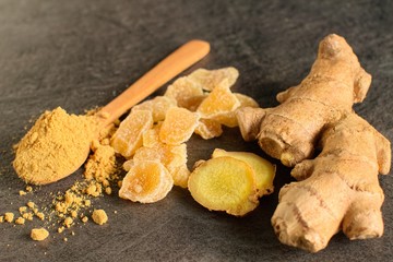 Ginger root, candied and ginger powder in wooden spoon over grey concrete background