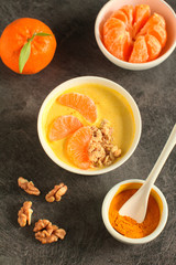 Tasty tangerine smoothie bowl with fruits, cereals, seeds and turmeric powder over grey background from above