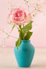 Delicate mini pink rose in a vintage blue vase on a tablein front of pink backgroud