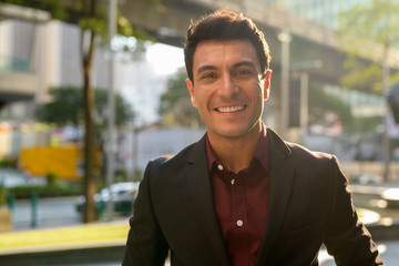 Face of happy young handsome Hispanic businessman smiling outdoors