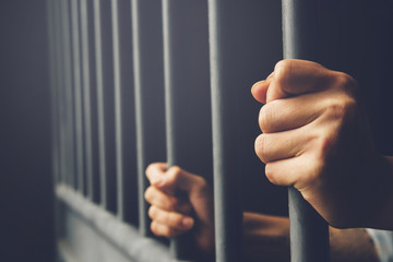 Man in prison hands of behind hold Steel cage jail bars. offender criminal locked in jail. filter dark vintage. - obrazy, fototapety, plakaty