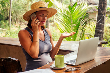 successful happy business lady using laptop and telephone freelancing on the tropical paradise beach. Girl cup tea coffee freelancer work sitting in a summer cafe remote work indian ocean