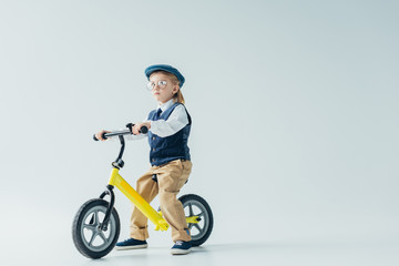 thoughtful kid in retro vest and cap riding bicycle and looking away