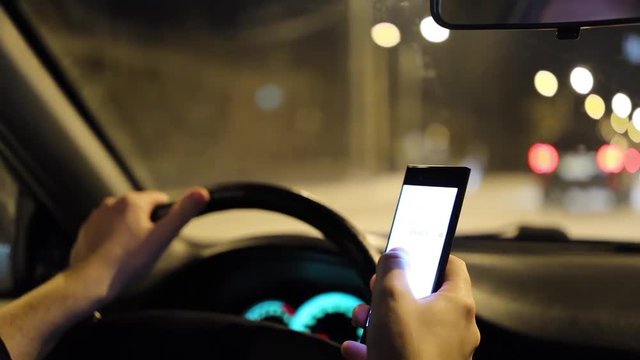 Man texting with a smartphone and driving car at night