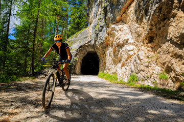 Single mountain bike rider on electric bike, e-mountainbike rides up mountain trail. Man riding on bike in Dolomites mountains landscape. Cycling e-mtb enduro trail track. Outdoor sport activity.