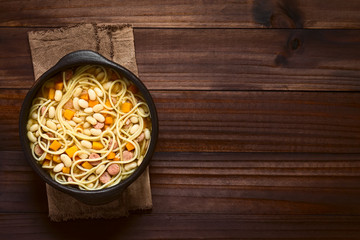 Chilean traditional Porotos con Riendas (beans with reins) dish of cooked dried beans with pumpkin, onion, spaghetti and sausage, photographed overhead on dark wood with natural light