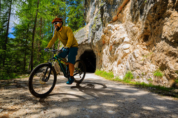 Single mountain bike rider on electric bike, e-mountainbike rides up mountain trail. Man riding on bike in Dolomites mountains landscape. Cycling e-mtb enduro trail track. Outdoor sport activity.