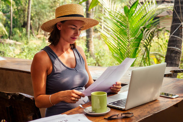 Technology and travel. Working outdoors. Freelance concept. Pretty young woman in hat using laptop in cafe on tropical beach.Hooray victory success and successful deal concept promotion at work