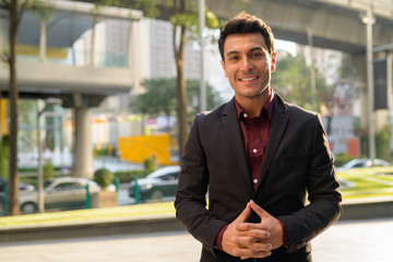 Young happy Hispanic businessman smiling in the city streets
