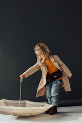  child in trench coat and jeans playing with umbrella on black background