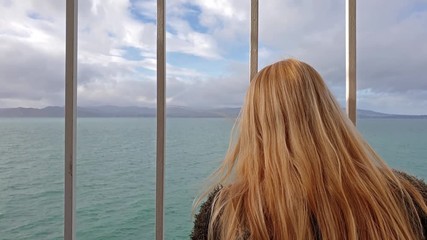 Blond Lady holding the bars and looking to sea and land