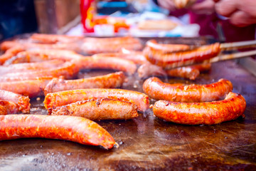 Turning delicious juicy sausages on barbecue plate with handle