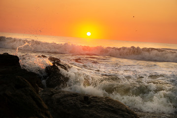 An orange colored sky at sunrise as the waves are crashing against the rocks at Marineland in St. Augustine, Florida.
