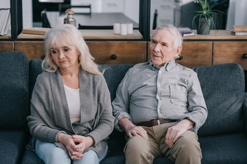 sad lonely senior couple in casual clothes sitting on couch at home