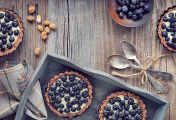 Top view on wholegrain blueberry tarts with vanilla cream on rustic wood