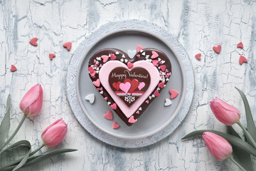 Valentine heart cake with chocolate, sugar decorations and text "Happy Valeitine" and a bunch of pink tulips