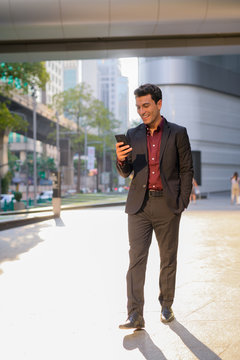 Happy Young Handsome Hispanic Businessman Using Phone Outside The Office Building