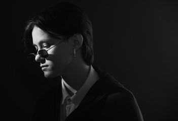 Serious, beautiful girl with short hair sitting in sunglasses under bright light on dark background