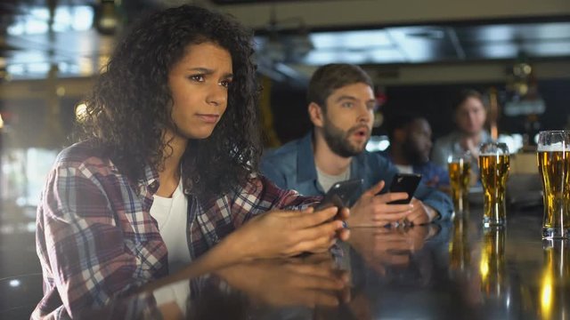 Young people in pub monitoring online bets in cellphone, upset about money loss