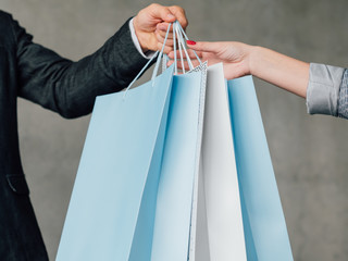 Fashion shopping. Female casual lifestyle. Checkout man handing over paper bags to woman. Cropped shot.