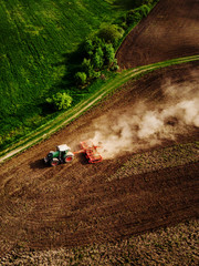 Tractor cultivating field, kicking up rocks and dust in early morning - obrazy, fototapety, plakaty