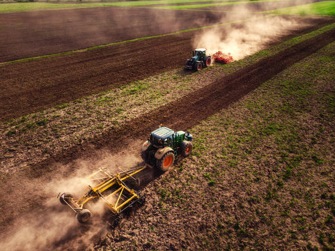 Tractor cultivating field, kicking up rocks and dust in early morning