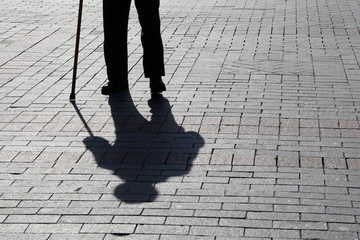 Silhouette of man walking with a cane, long shadow on pavement. Concept of lame or blind person,...