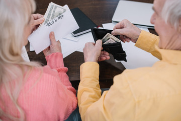 back view of senior couple holding money and envelope with 'roth ira' lettering while sitting at table