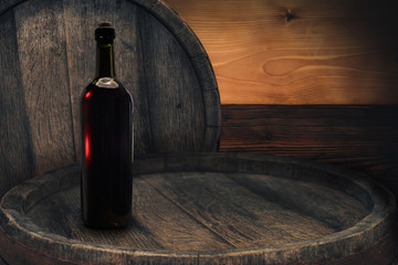 Red wine bottle on a old barrel table background wood wall.