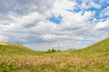 Spring landscape with a ravine and wires of power lines against the sky with clouds