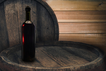 Red wine bottle on a old barrel table background wood wall.