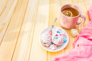 Romantic sweet breakfast concept. Green tea, lemon, meringue (cake). On wooden background with pink cloth.