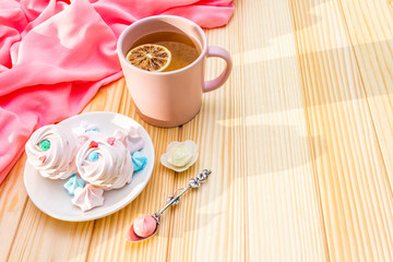 Romantic sweet breakfast concept. Green tea, lemon, meringue (cake). On wooden background with pink cloth.