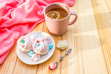 Romantic sweet breakfast concept. Green tea, lemon, meringue (cake). On wooden background with pink cloth.