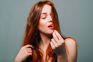 Young fashion model portrait. Redhead beauty. Woman with auburn hair. Closed eyes. Glitter freckles makeup. - obrazy, fototapety, plakaty