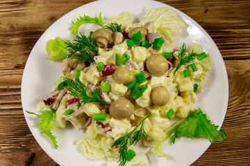 Potato salad with marinated mushrooms, eggs, red onion and mayonnaise on wooden table