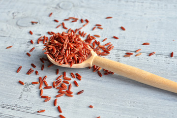 red rice on wooden spoon over wooden background
