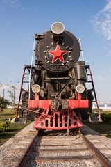 An old steam locomotive with red wheels and a red star stands in an open-air Museum on the seaside Boulevard embankment in Baku, Azerbaijan.