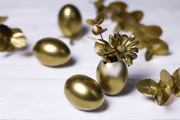 Golden eggs, decorative leaves and flowers on white vintage background.