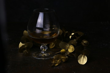 Glass with alcohol and golden floral design elements. Cognac Decanter on dark background. Carafe of...