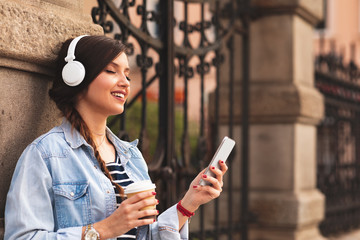 Young woman listens to music via headphones and smartphone in the city