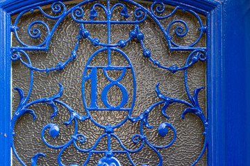 House number 18 with the eighteen worked in metal in a decorative metal grating in front of a glass pane on a blue door