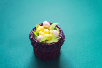 Easter composition with traditional decor. Small colorful eggs in wicker basket on soft background.