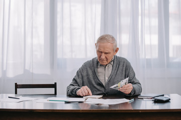 Senior man sitting at table with paperwork and using calculator while counting money